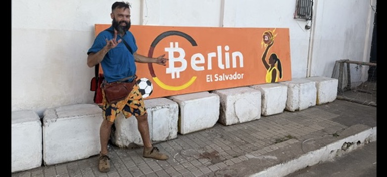 TJ Murphy standing beside the completed orange Berlín El Salvador sign at the basketball court.